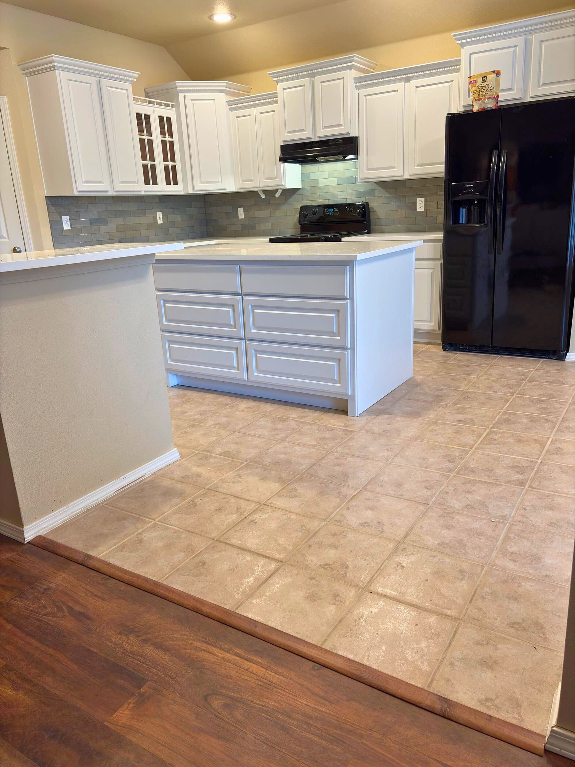 Painted kitchen cabinets and a new center island with drawer storage and a quartz countertop, with existing tile flooring.